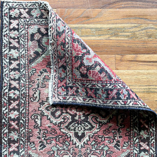 Woven Persian mini rug in in red, brown, and cream with one corner folded over to show woven underside.