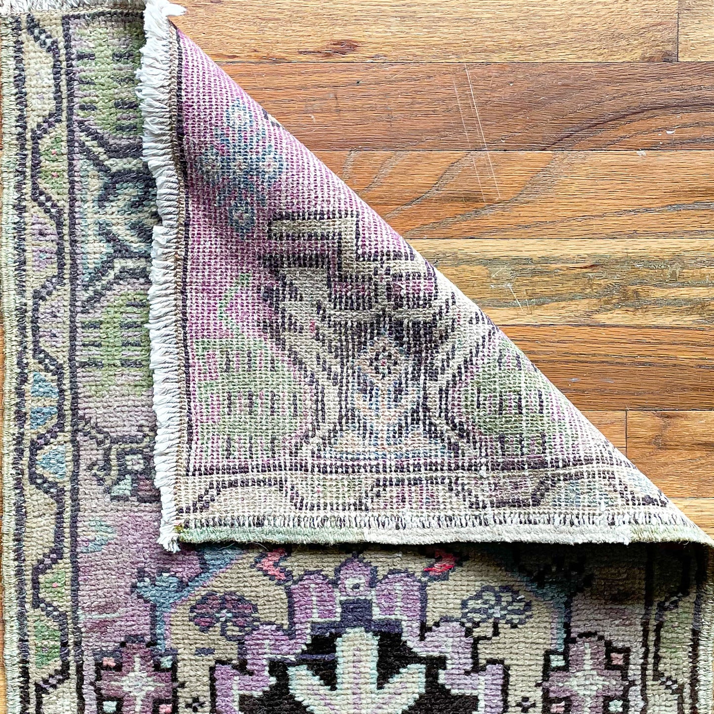 Woven Turkish mini rug in purple, green, and black with one corner folded over to show woven underside.