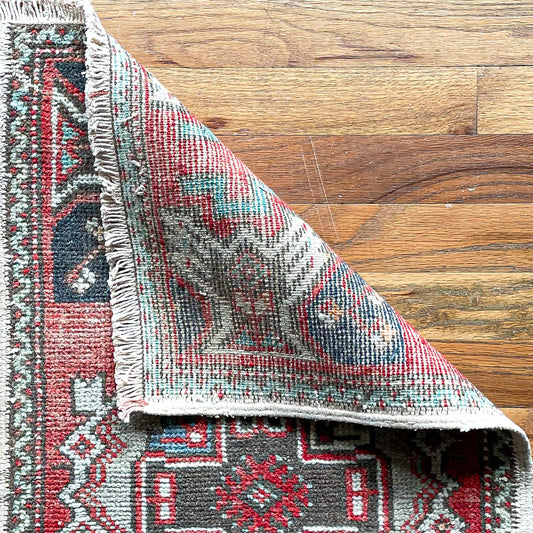 Woven Turkish mini rug in red, brown, and cream with one corner folded over to show woven underside.